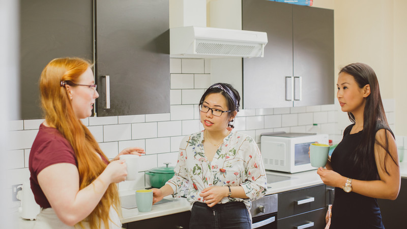 Three students chat to each other in their kitchen